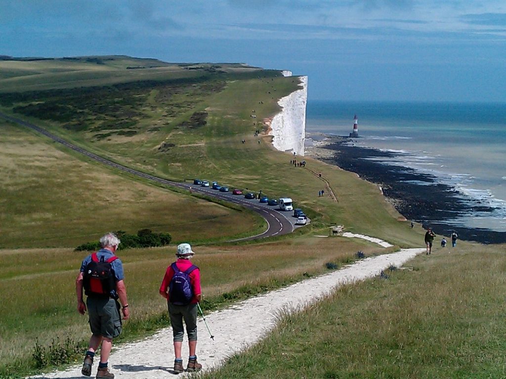 Two walkers heading along the clifftops towards Beach Head with the sea and the lighthouse in the distance